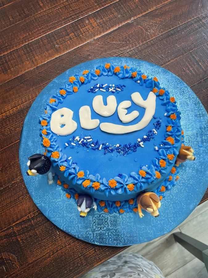 Blue round Bluey birthday cake with orange flowers and character figures